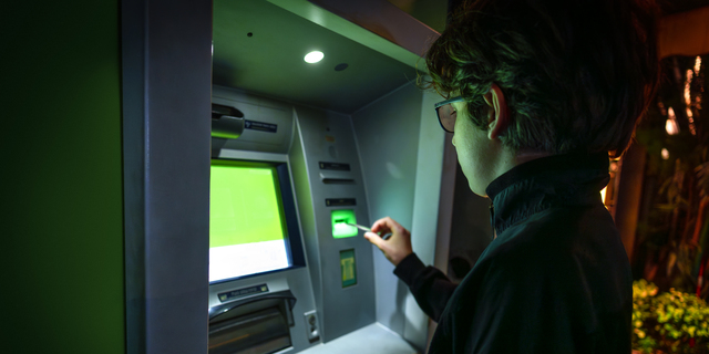 Teenager inserting bank card into ATM machine
