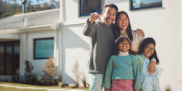 An Asian family stands smiling together holding house keys in front of a home