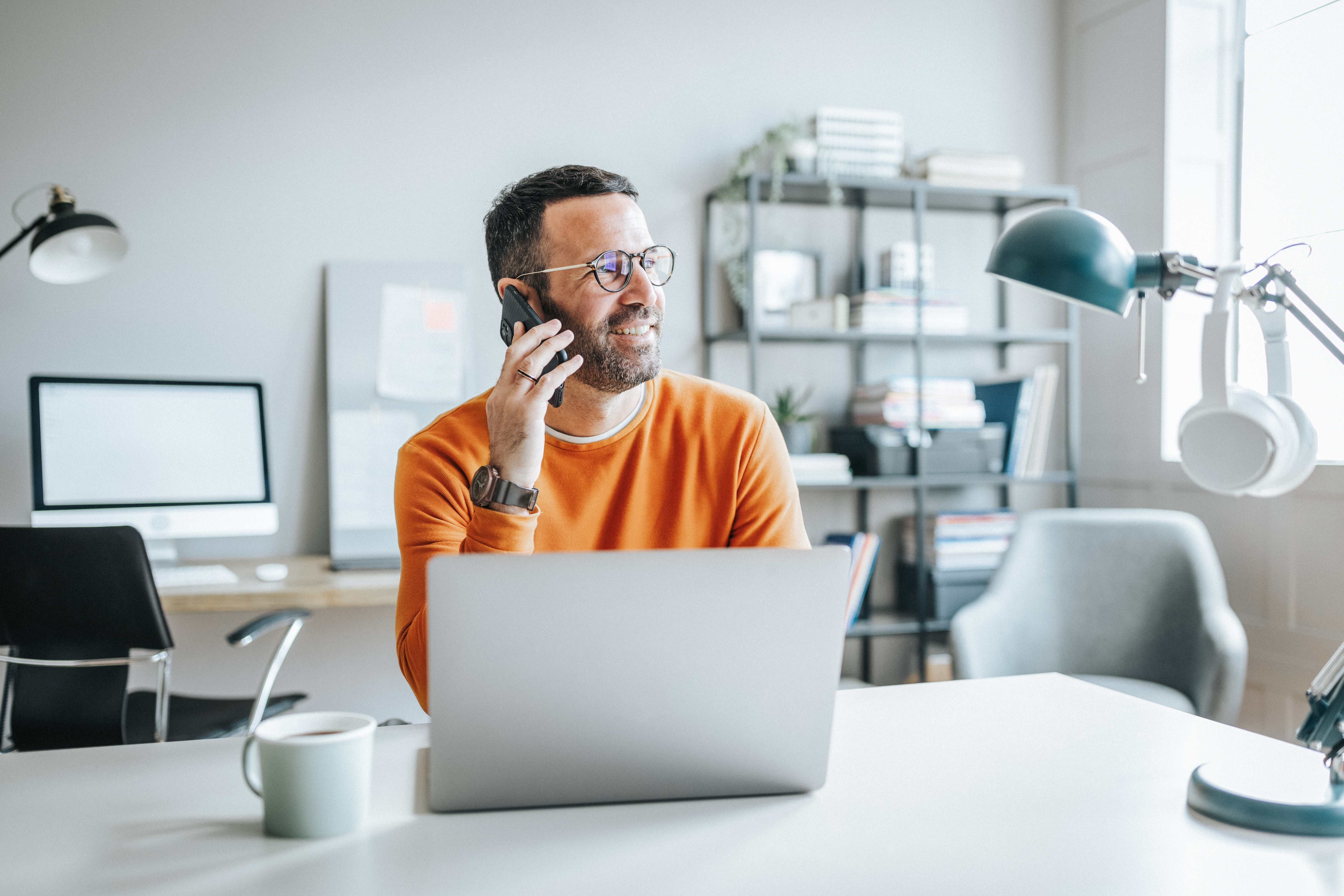 Man on his phone while sitting at a desk on his laptop