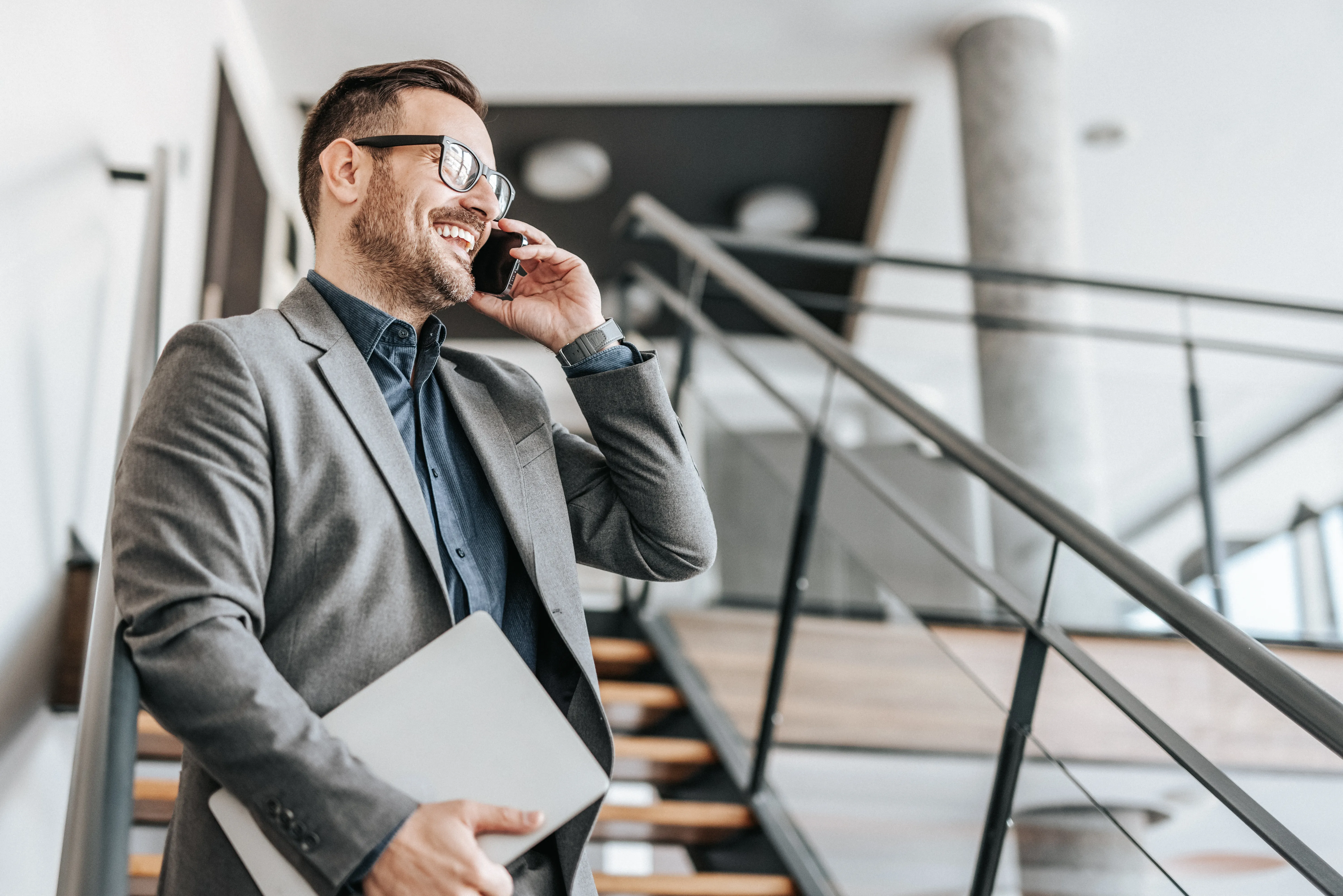 Smiling businessman talking on phone walking down staircase in open office 
