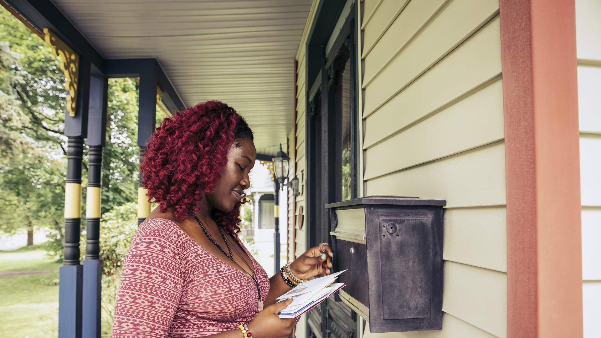 Young woman in red dress checking mail on front porch