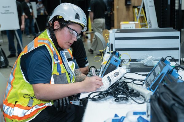 Female cabling technician in a hard hat and safety vest logging test results at a the BICSI Cabling skills competition
