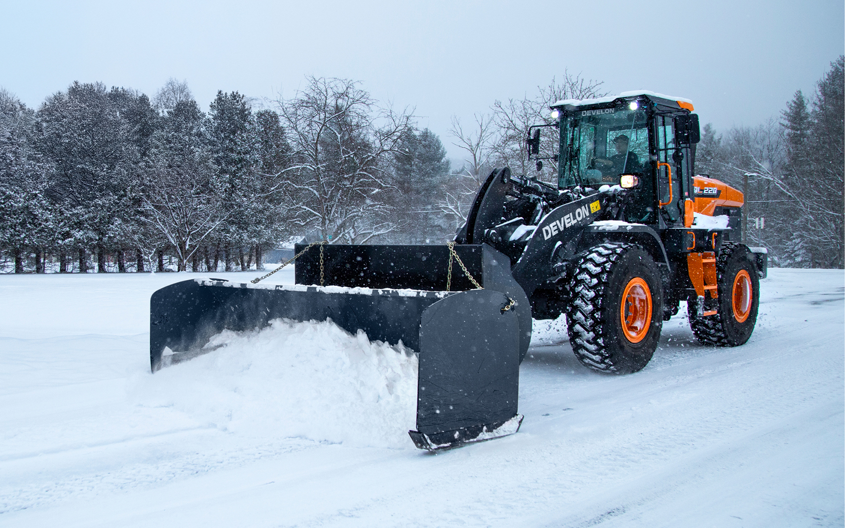 A DEVELON wheel loader clears snow using a snow pusher attachment.