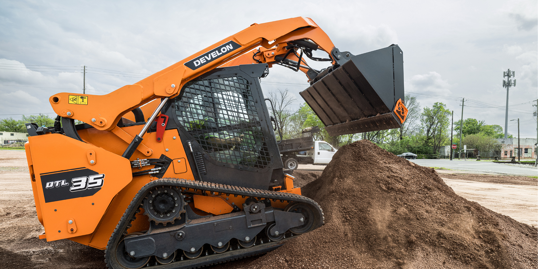 A DEVELON compact track loader dumps a pile of dirt at a job site.