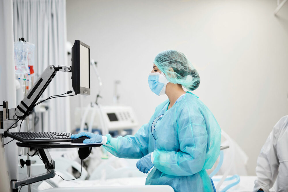 Picture of healthcare worker in full PPE gear, scrubs and mask at computer terminal