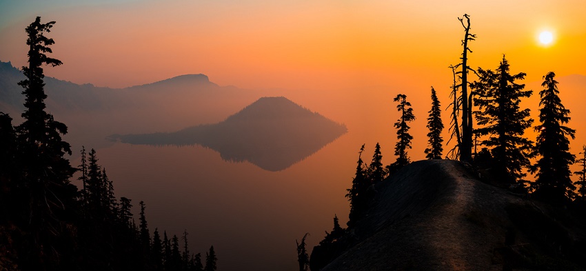 A hazy view of Crater Lake at sunrise, with deep shadows and bright orange colors