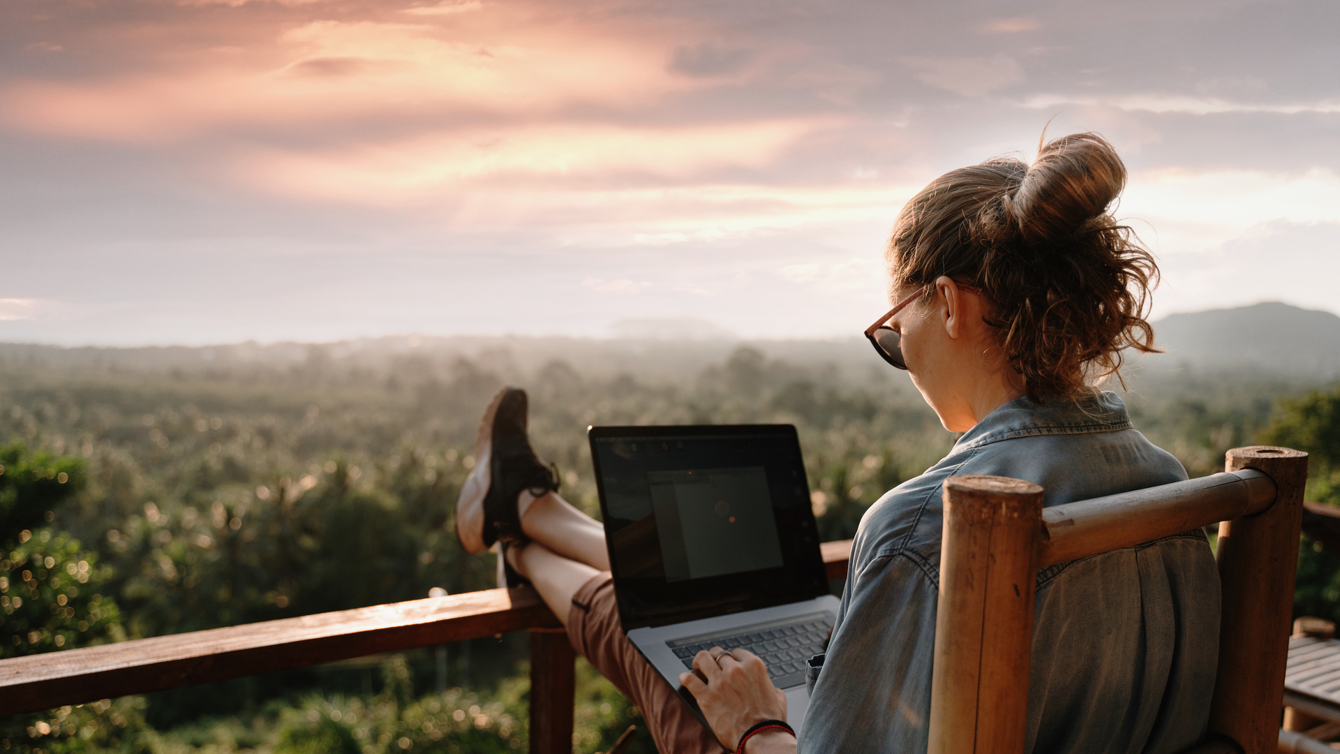 Young business woman working at the computer in cafe on the rock. Young girl downshifter working at a laptop at sunset or sunrise on the top of the mountain to the sea, working day.