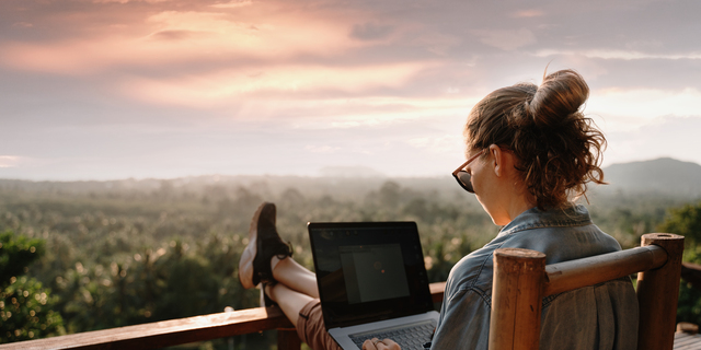 Young business woman working at the computer in cafe on the rock. Young girl downshifter working at a laptop at sunset or sunrise on the top of the mountain to the sea, working day.