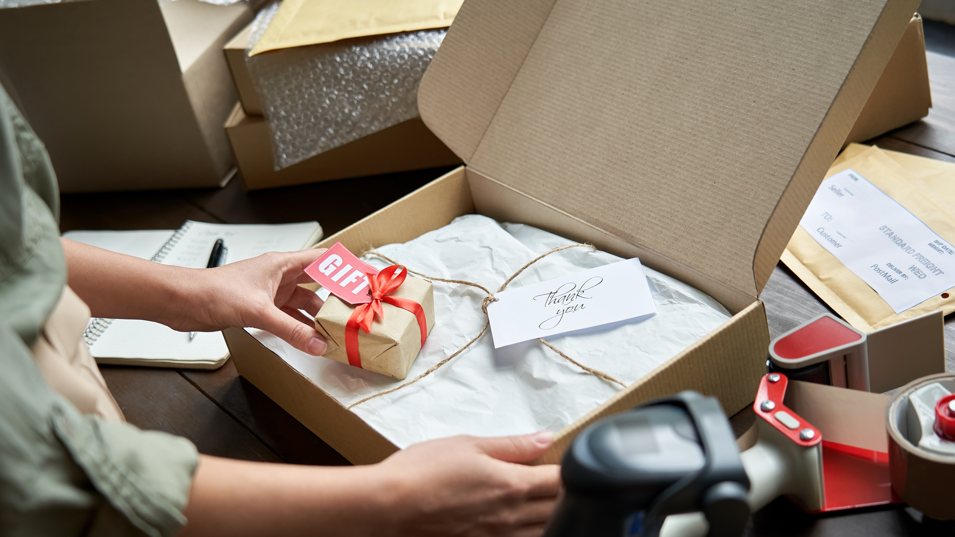 Female online store small business owner seller holding gift packing package post shipping box preparing delivery parcel on table. Ecommerce dropshipping holiday presents sale concept. Closeup.