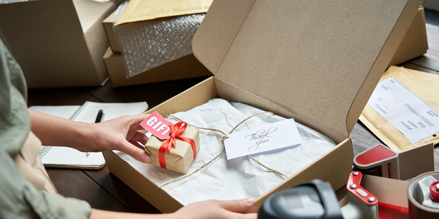 Female online store small business owner seller holding gift packing package post shipping box preparing delivery parcel on table. Ecommerce dropshipping holiday presents sale concept. Closeup.