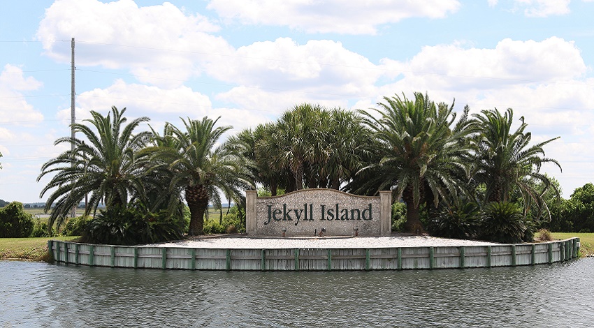 A sign reading Jekyll Island surrounded by ocean water and lush plants