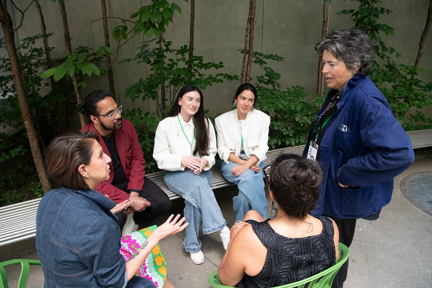 In a courtyard, a woman in a jean jacket and one in a blue jacket converse while students Irmak Senyurt and Lucía Jaramillo and another woman and a male professor listen.