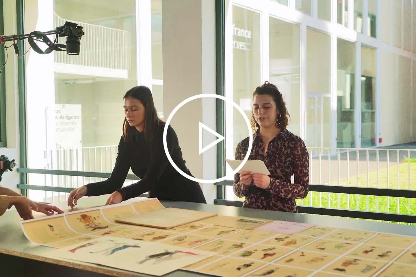 Two Students Stand Before Caricatured Images On A Table