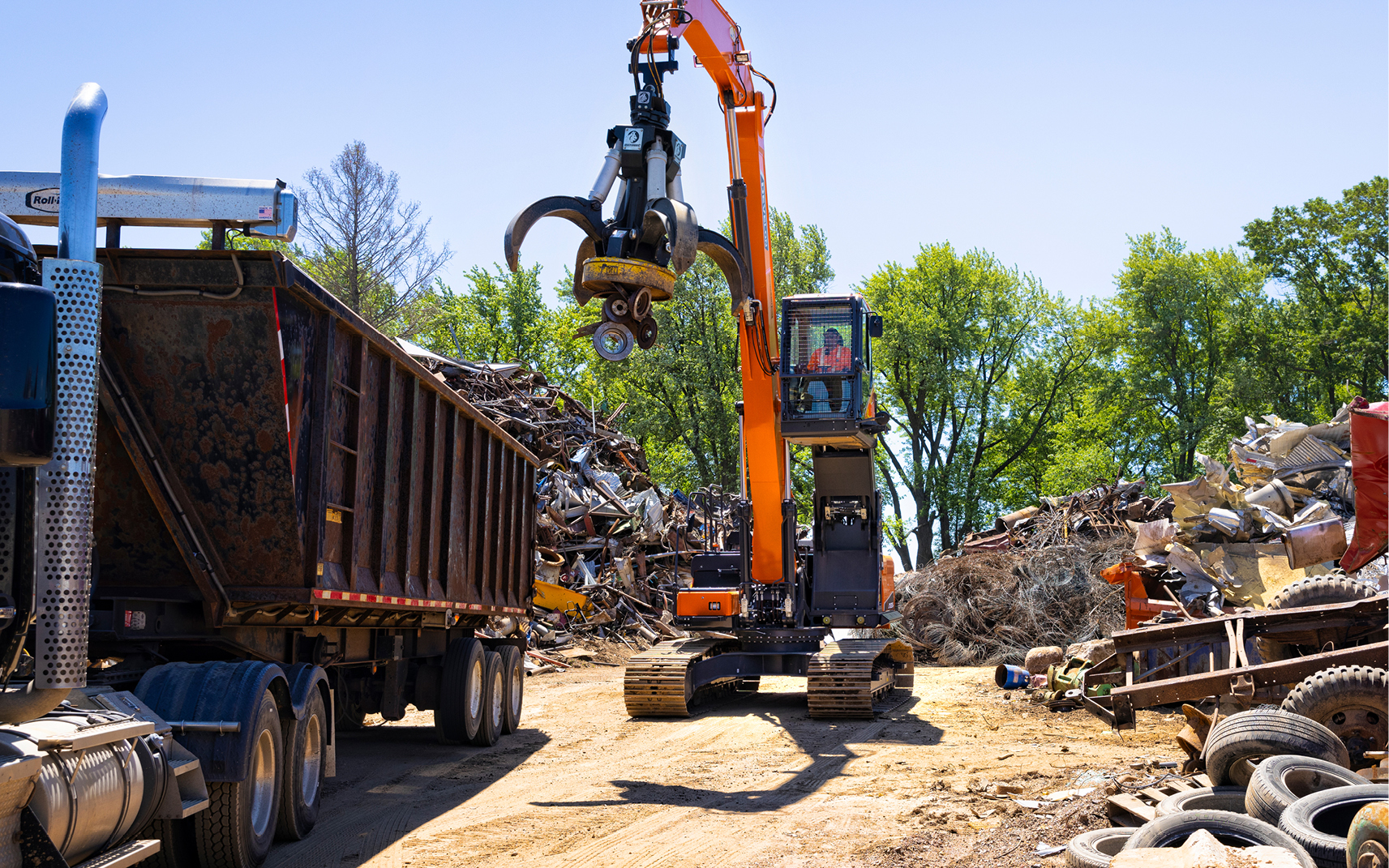 A material handler uses a magnet attachment to load metal into a trailer.