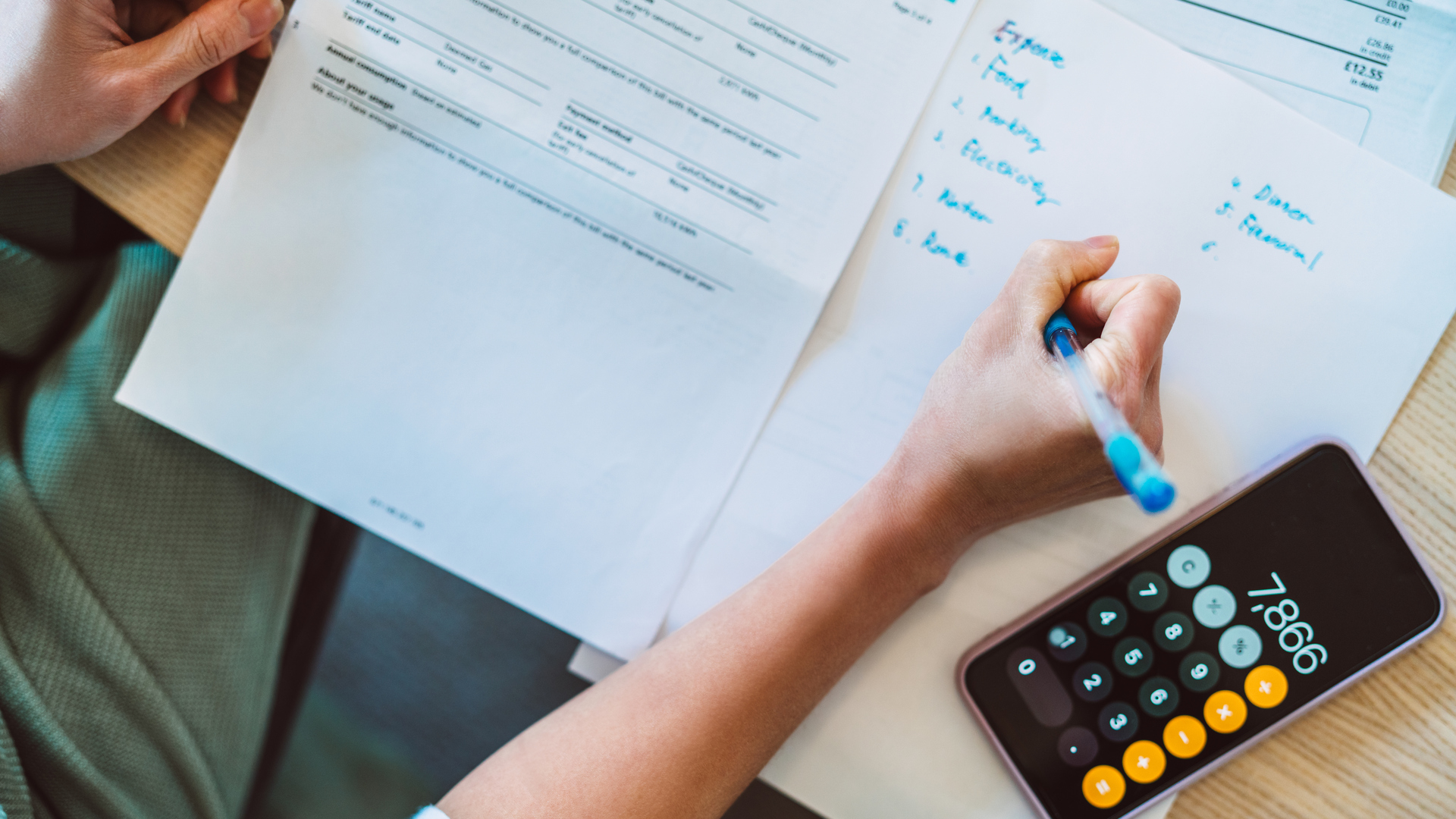 Overhead view of young Asian women managing home finance using smartphone. She is working with household utility bill and  calculating expenses at home.