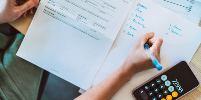 Overhead view of young Asian women managing home finance using smartphone. She is working with household utility bill and  calculating expenses at home.