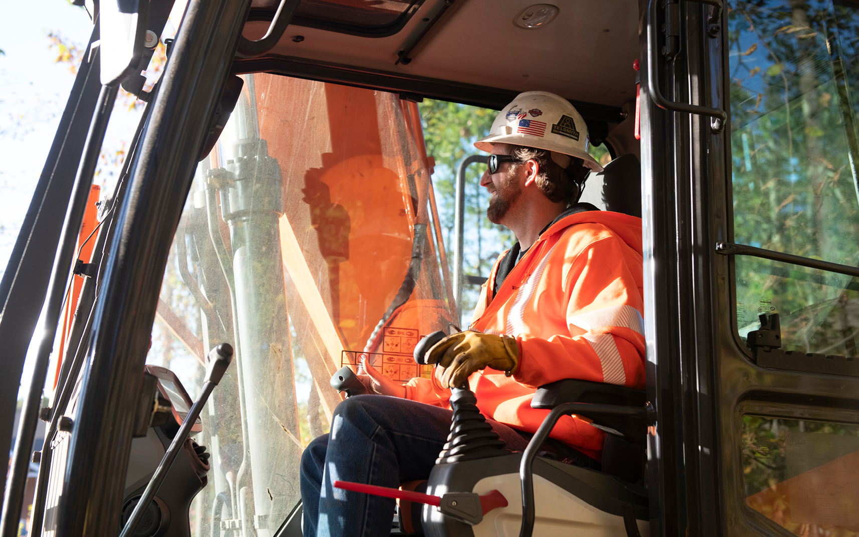 An excavator operator wearing PPE, including a hard hat and safety glasses.