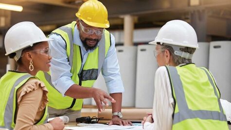 Project manager in a yellow hard hat reviewing site construction blueprints with two team members