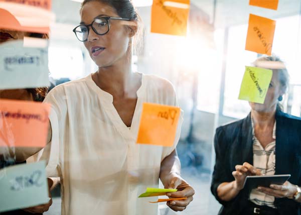 Woman writing on colorful sticky notes on a glass wall during a collaborative planning session.