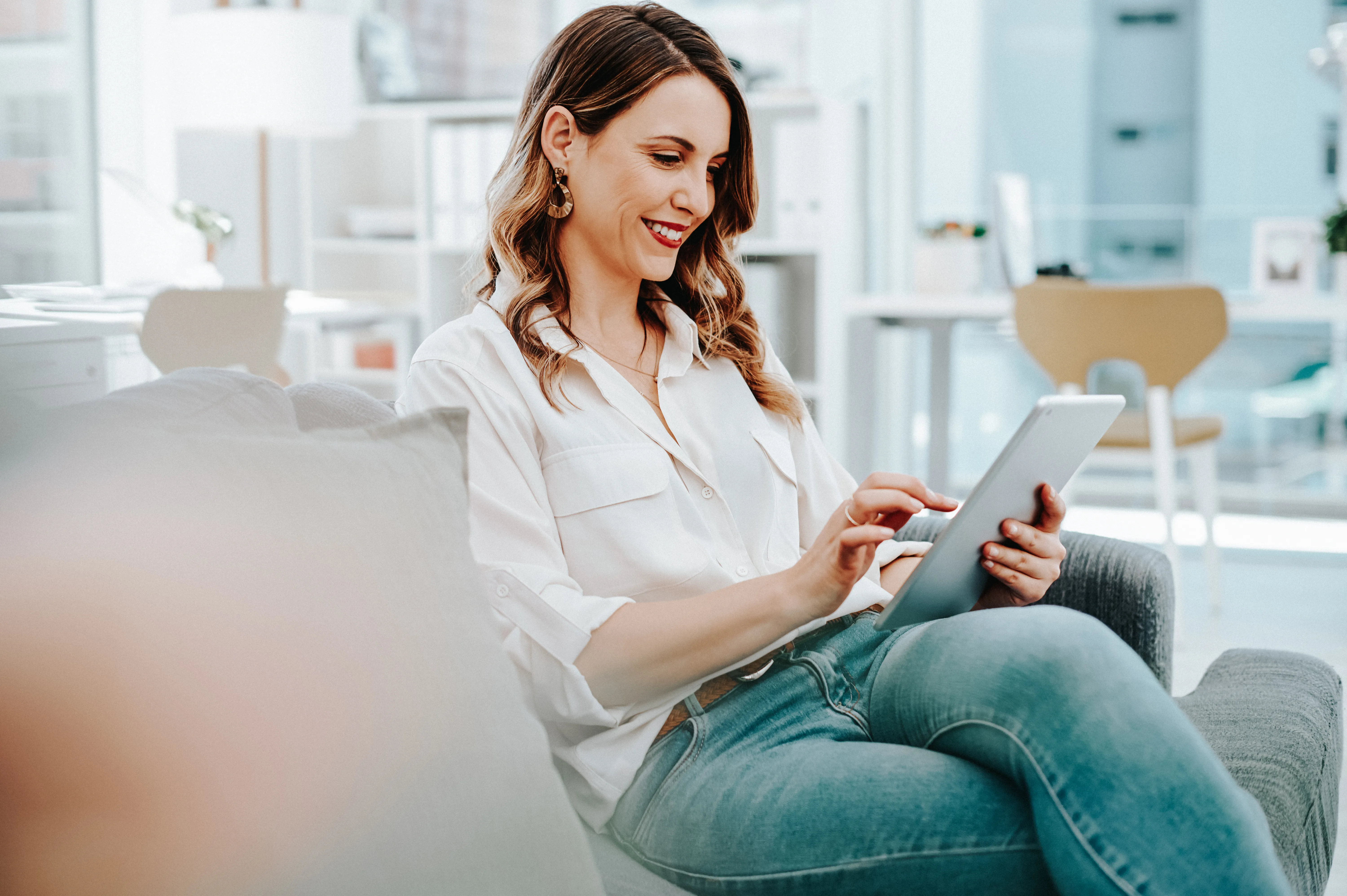 Woman seated on sofa in brightly lit office looking at tablet 