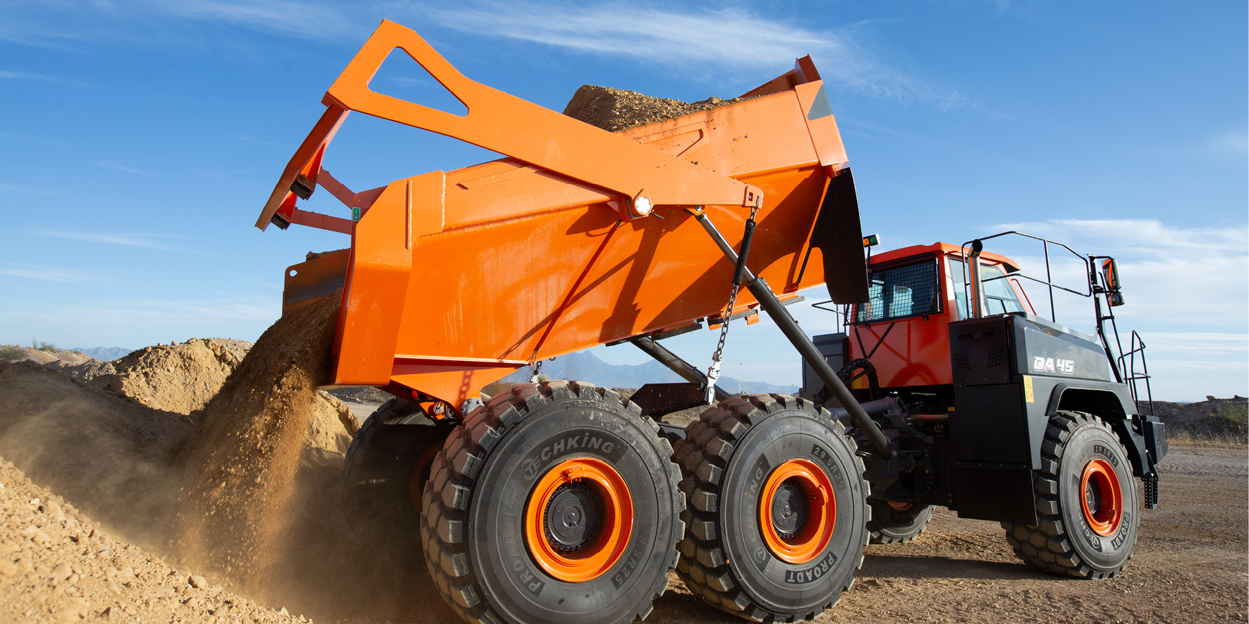 A DEVELON articulated dump truck dumps dirt at a job site.