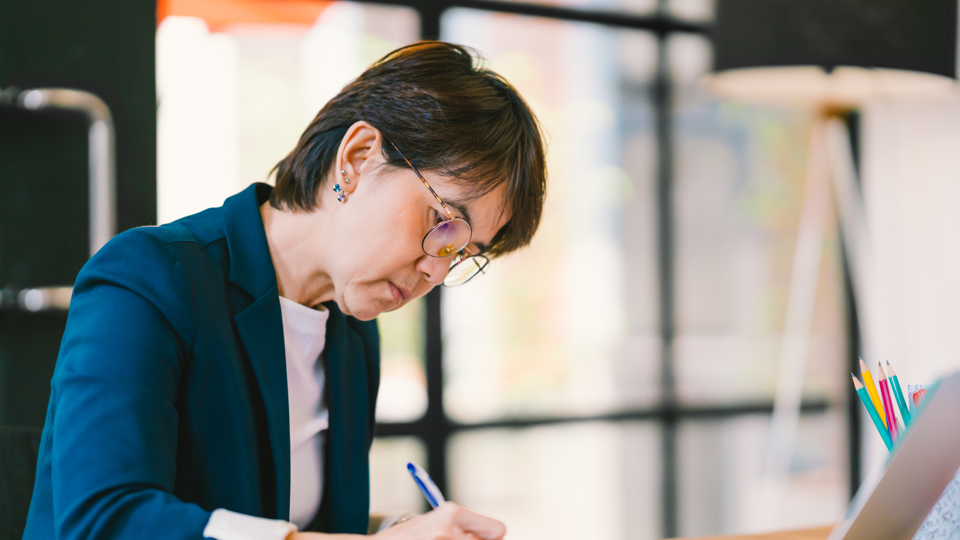 Beautiful middle age Asian woman working on paperwork in modern contemporary office, with laptop computer. Business owner, entrepreneur, executive manager, or employee office worker concept