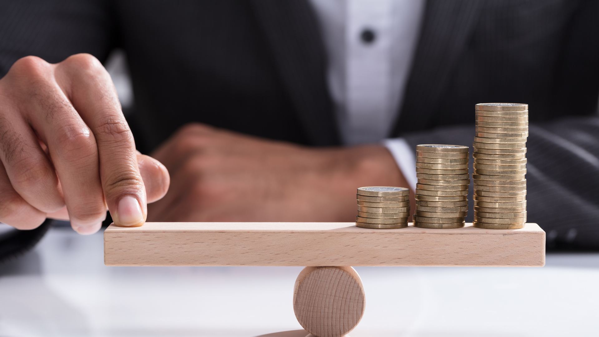 Businessperson Balancing Stacked Coins On Wooden Seesaw