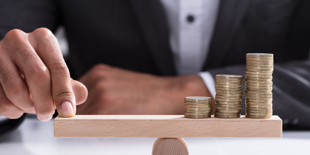 Businessperson Balancing Stacked Coins On Wooden Seesaw