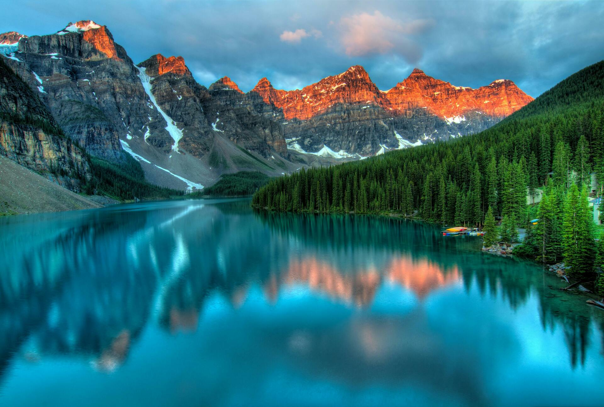 Mountains at sunrise reflecting on a clear lake in the foreground.