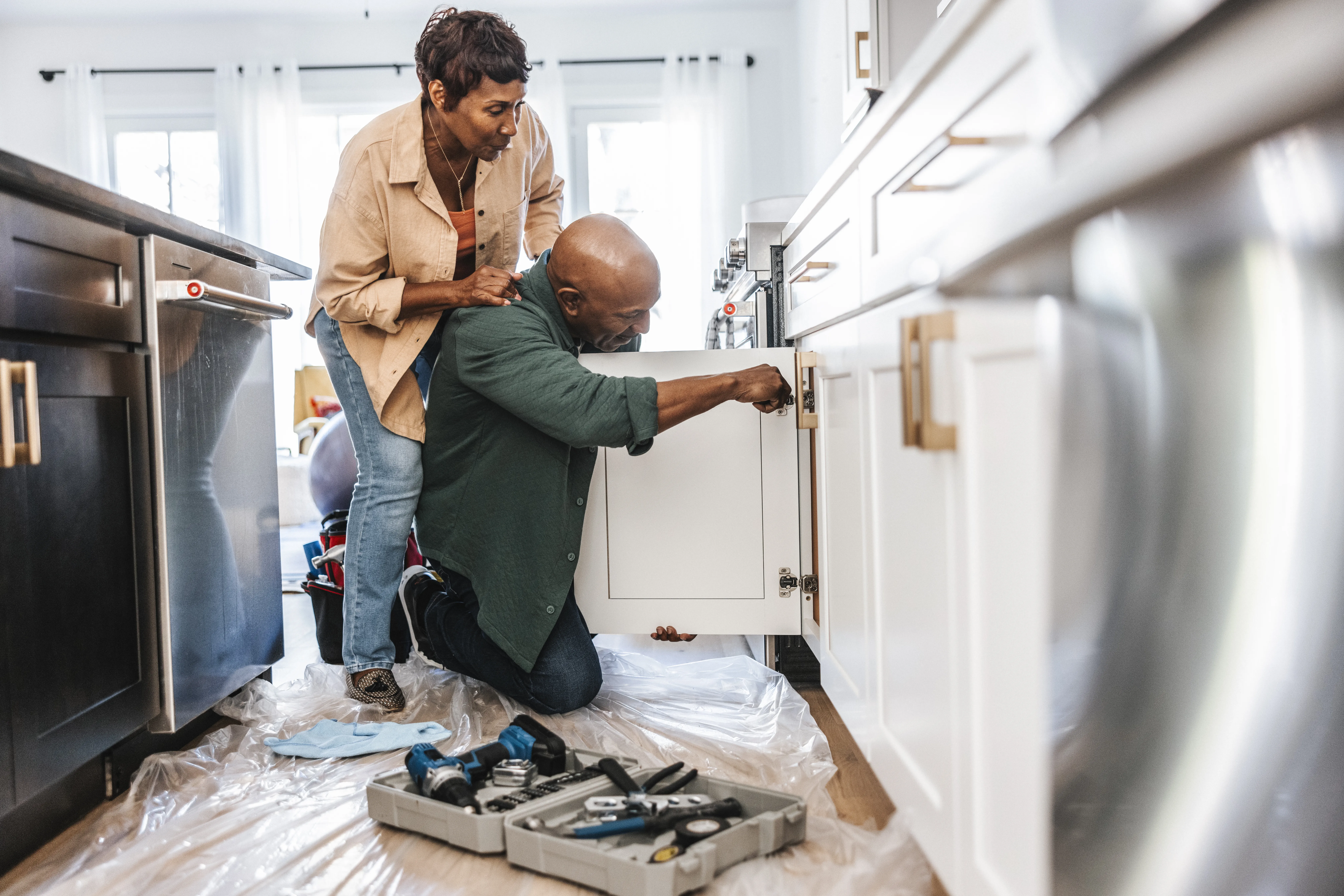 Senior couple repairing or installing white, kitchen cabinet doors in a residential home. 
