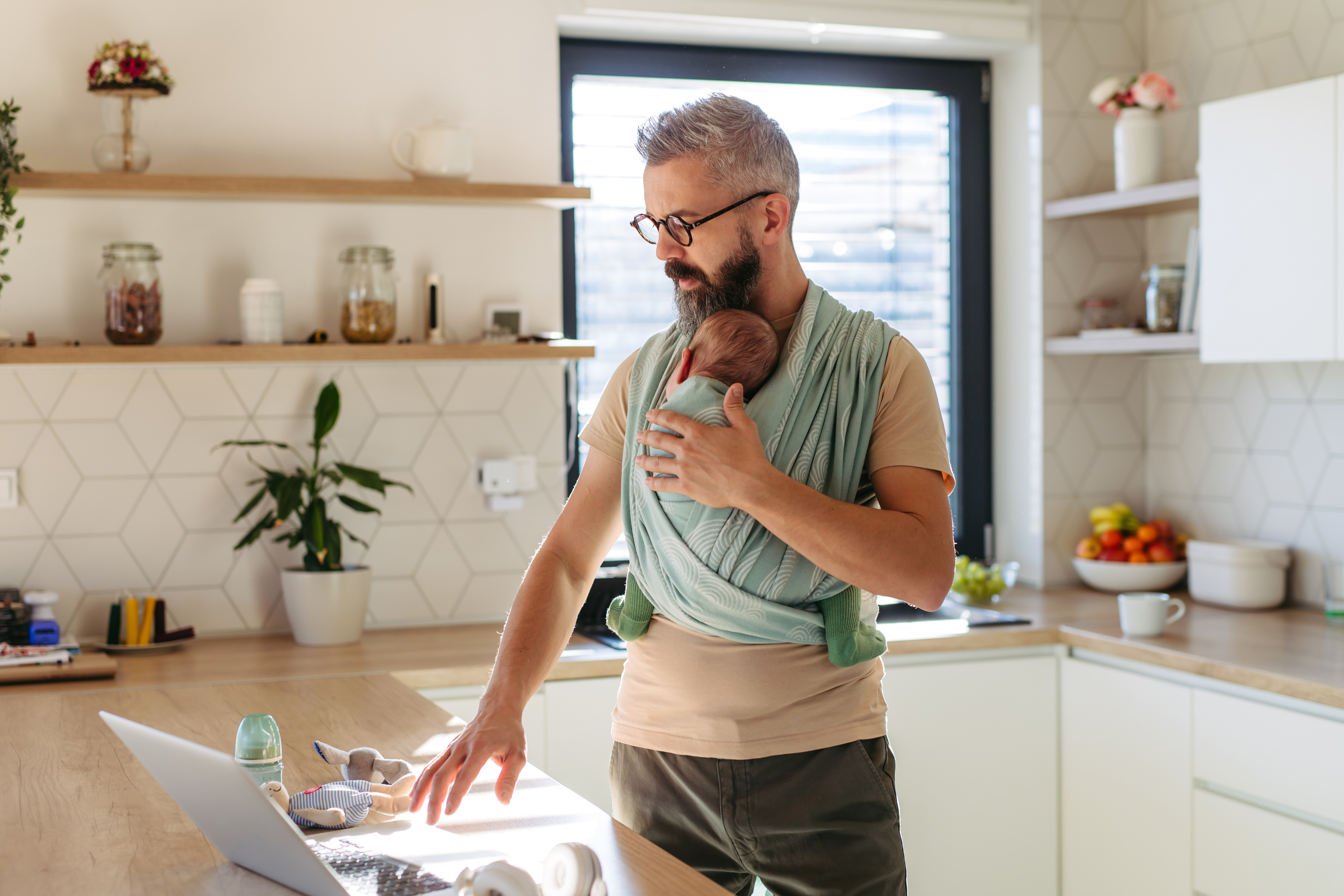 father holding baby while working from kitchen