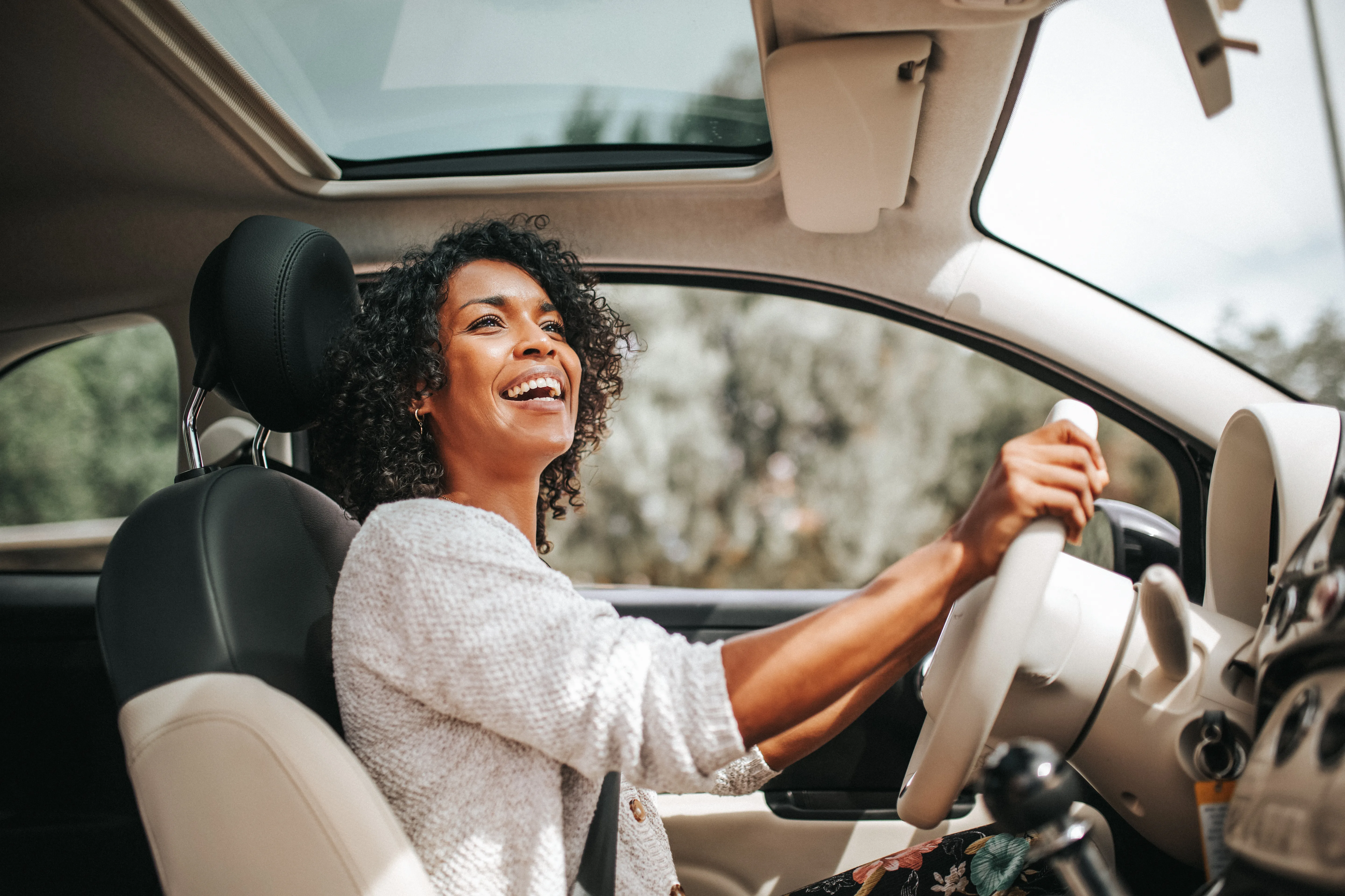 Smiling young African American woman driving car. 