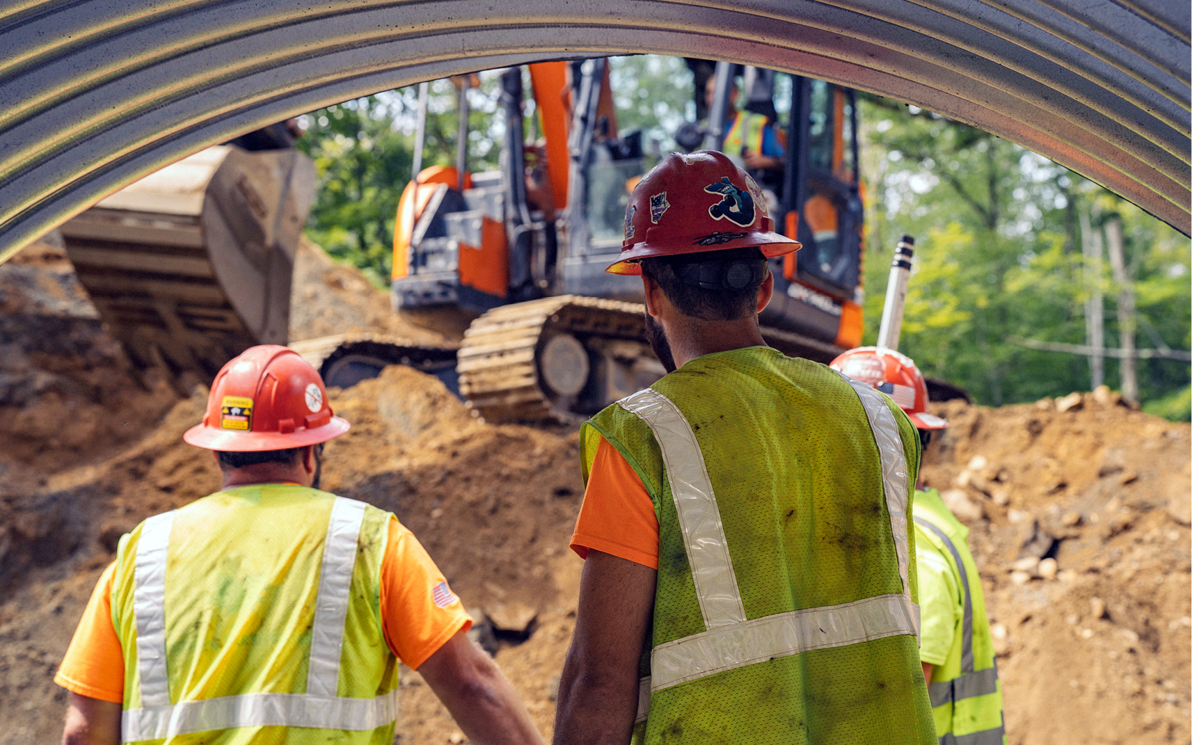 Three construction crew members looking towards a DEVELON excavator on a job site.