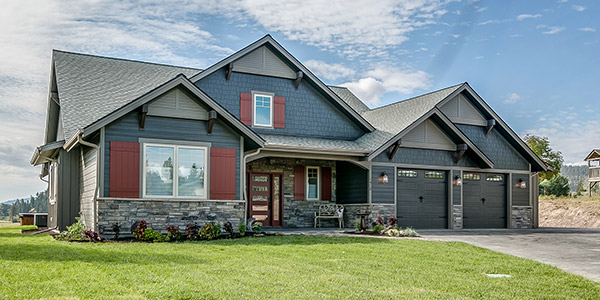 A nice ranch-style home with a dark blue exterior and red accents sitting on a well kept lawn