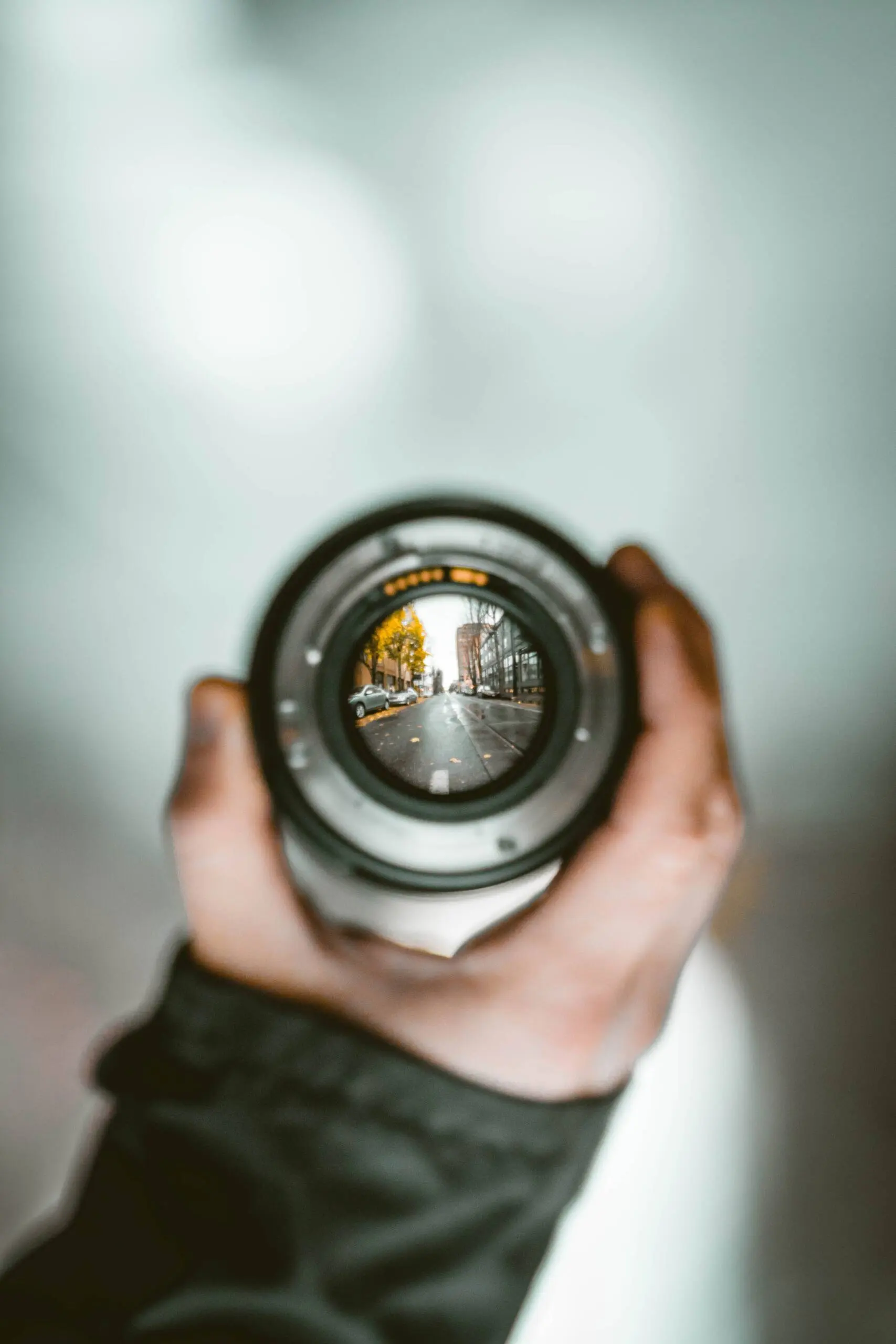 Hand holding a camera lens - the lens contains a view of a city street with pathways in Autumn