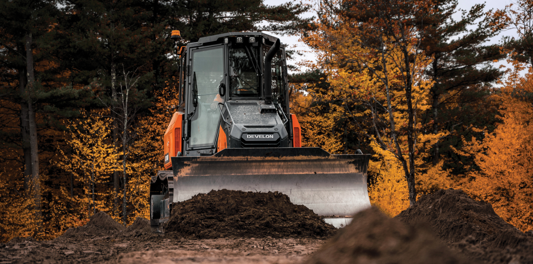 A DEVELON dozer pushes a pile of dirt on a job site.