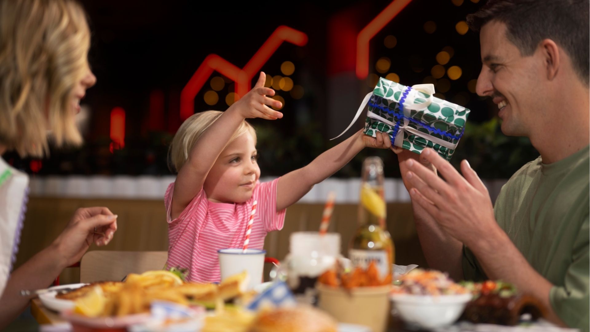 Dad receiving a wrapped Father’s Day gift  from a child while sharing a meal together.
