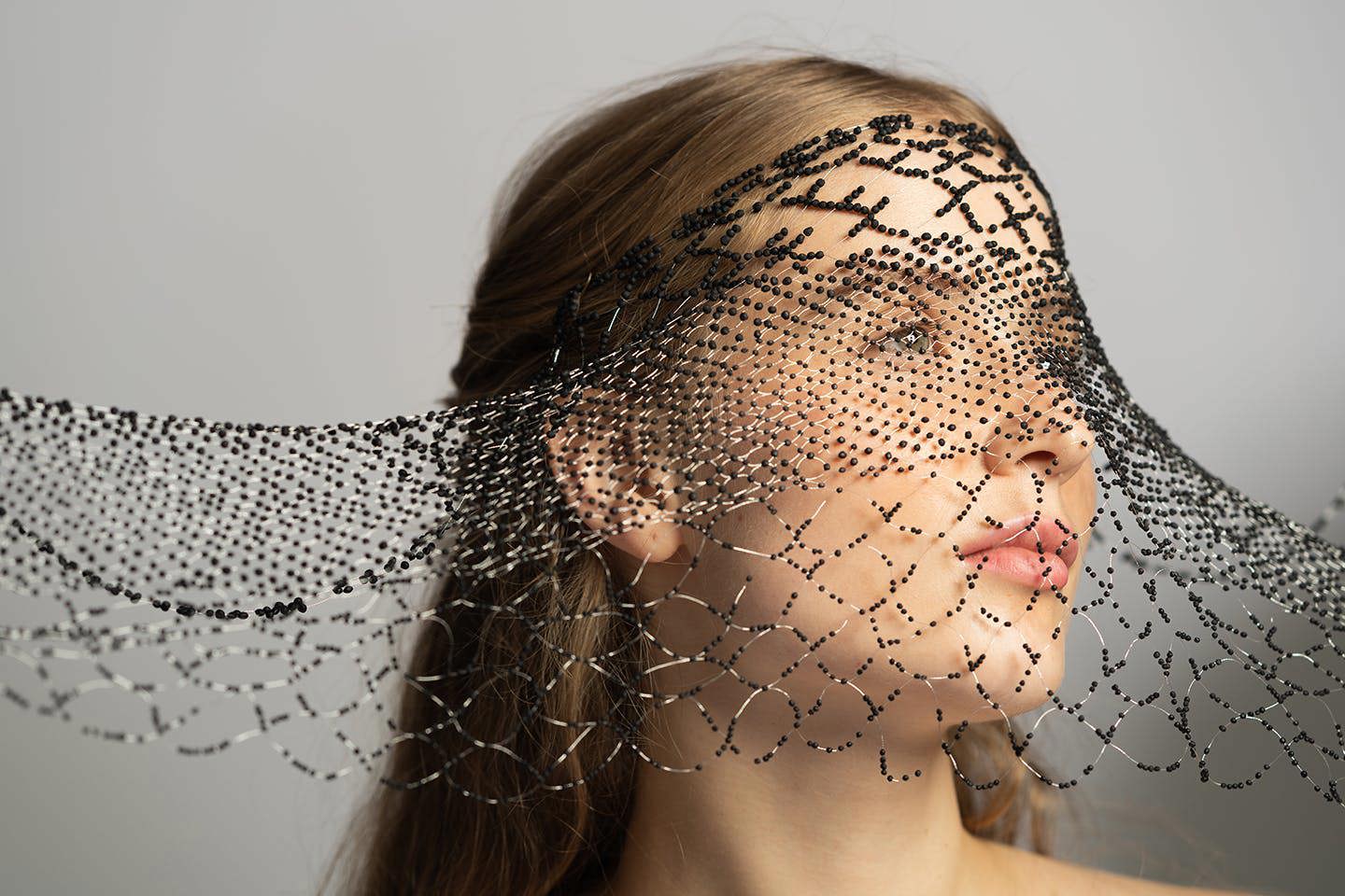 A portrait of a model holding a black and white beaded garment against their face.