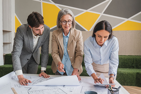 Design team and project managers reviewing architectural blueprints and tablet layouts in a modern office