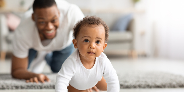 Happy Black Father Looking At Infant Baby Crawling On Floor At Home