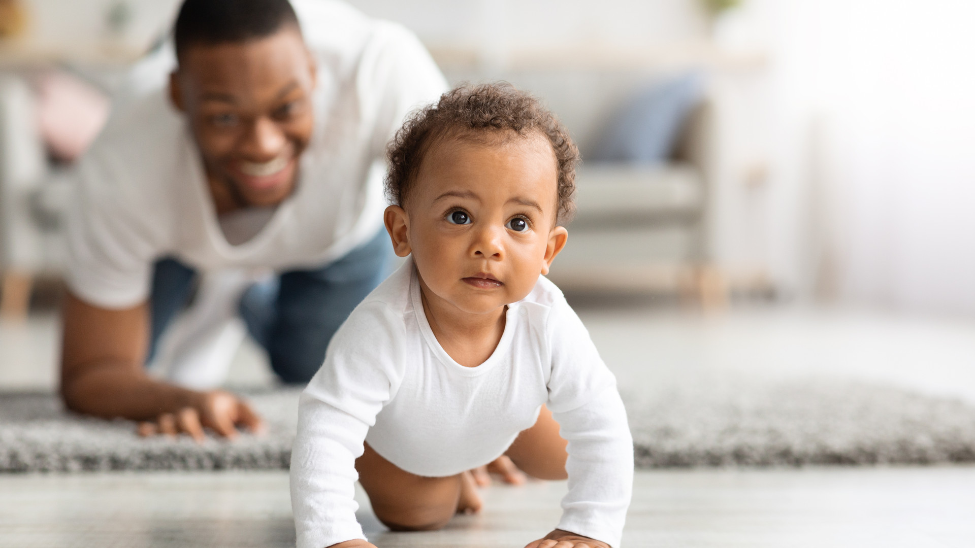 Happy Black Father Looking At Infant Baby Crawling On Floor At Home