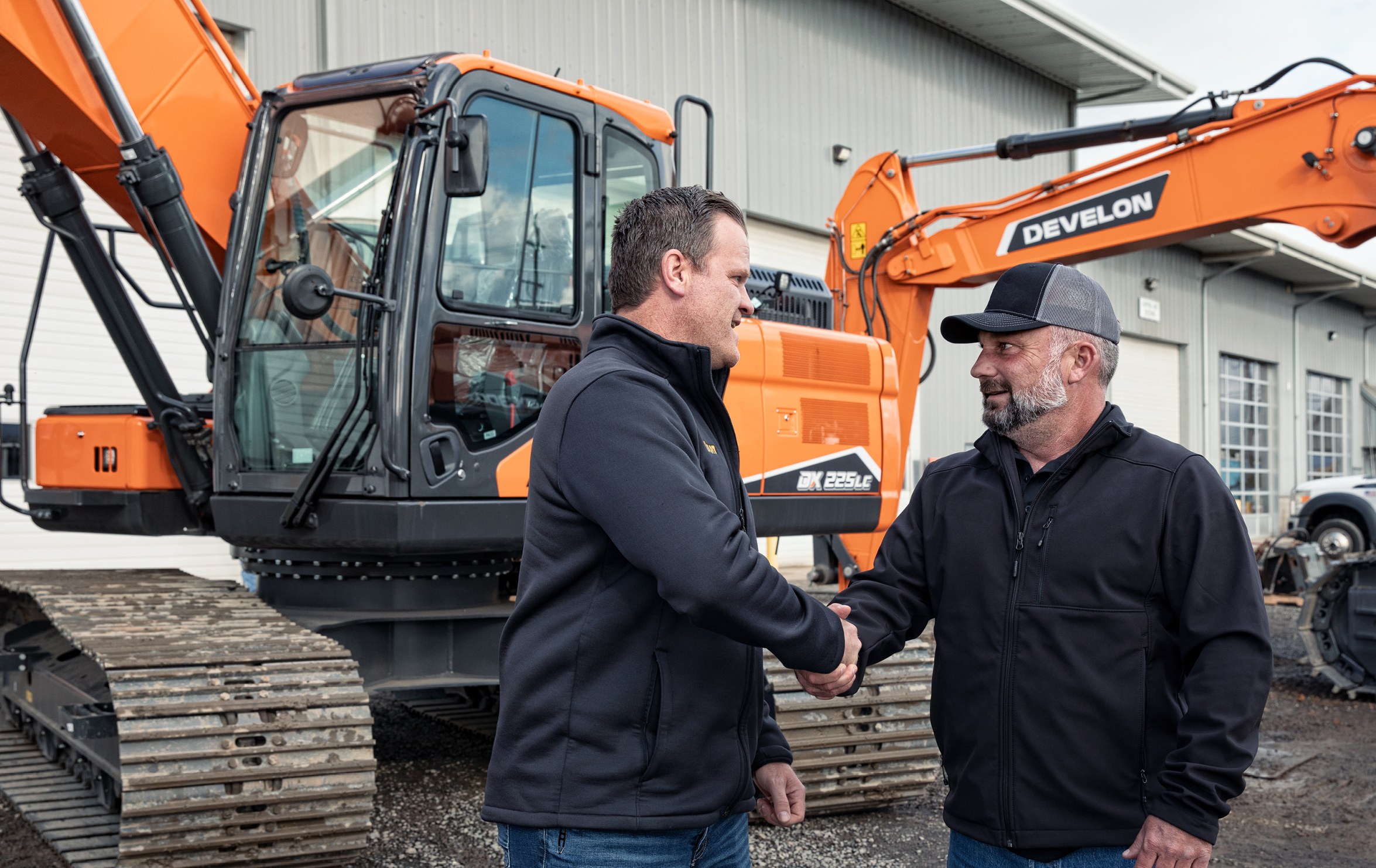 DEVELON National Accounts Team member and rental company owner shaking hands in front of a DEVELON excavator.