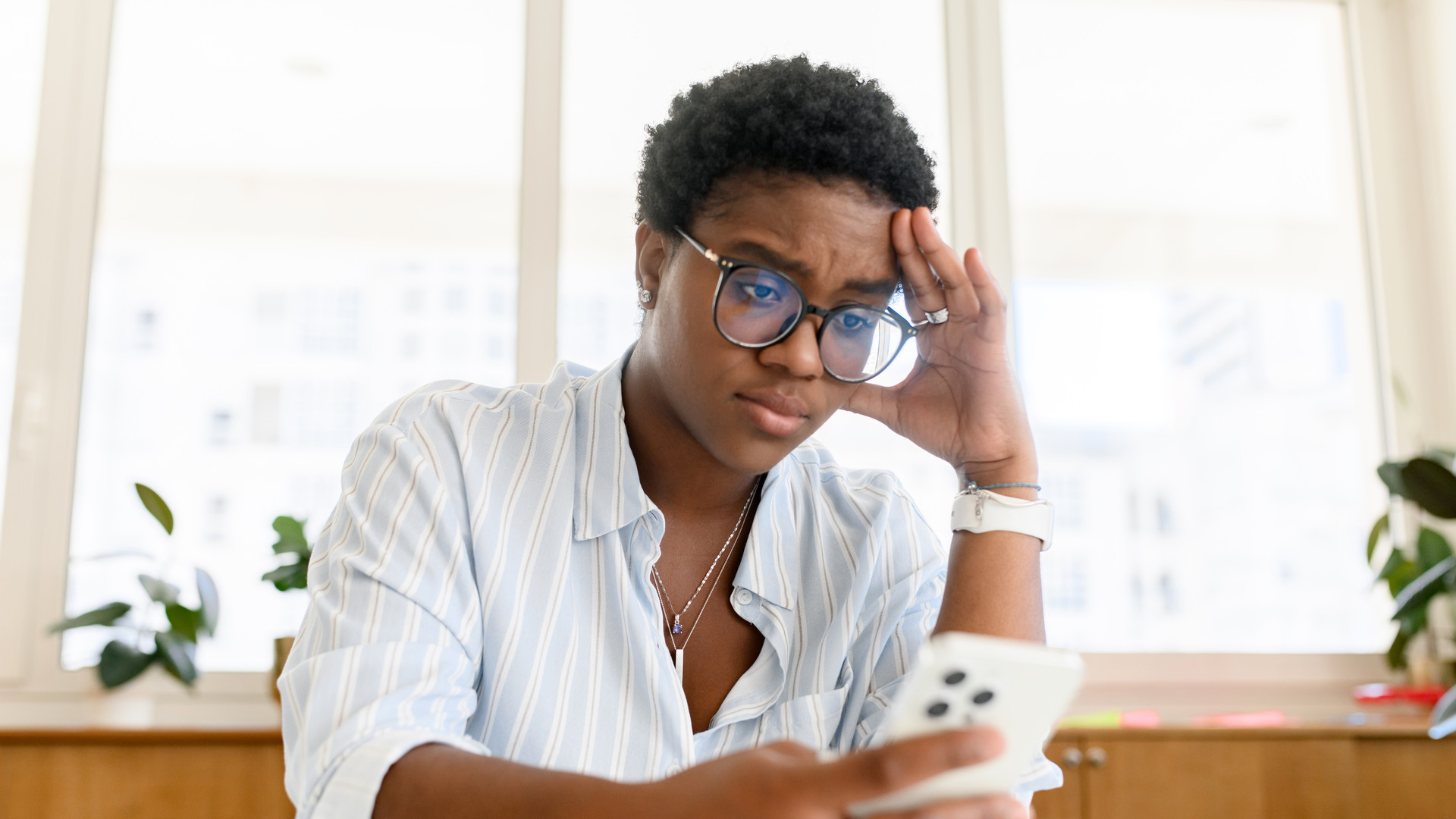 Sad and worried african woman looking at the smartphone screen, reading bad news, stressed female office employee receive emails about loan