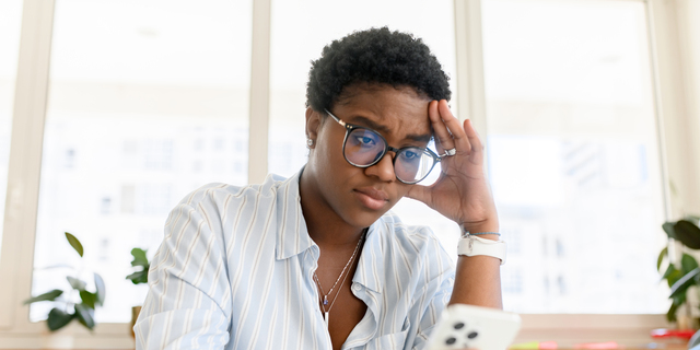 Sad and worried african woman looking at the smartphone screen, reading bad news, stressed female office employee receive emails about loan
