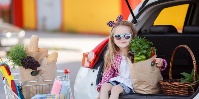 Little girl-the buyer of products, sitting in the open trunk of a car