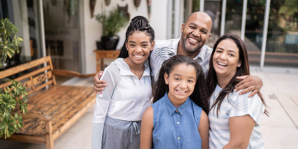 A Black family sits smiling together in front of a nice house 