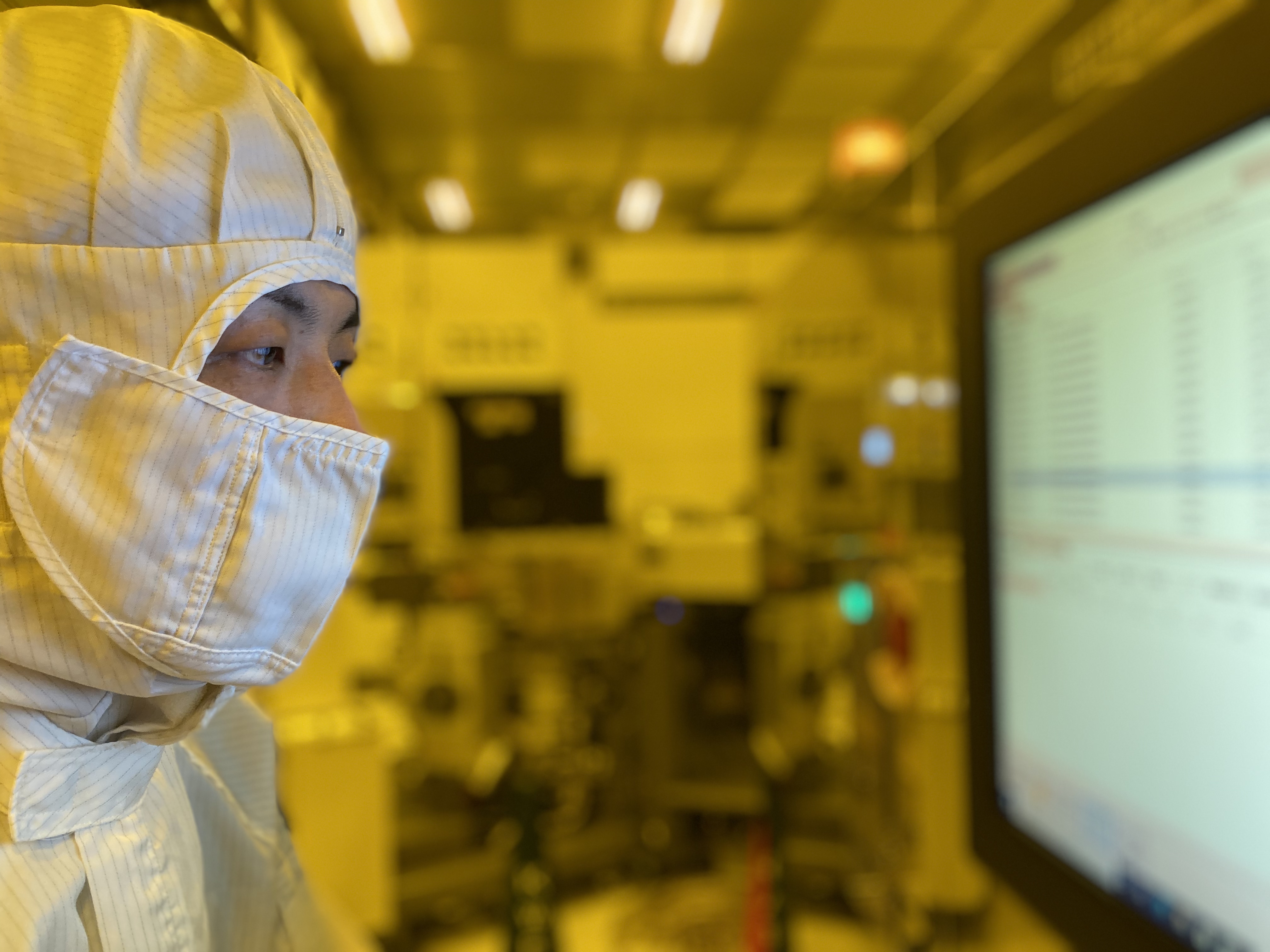 Taniguchi in the clean room, adjusting processing conditions for manufacturing equipment