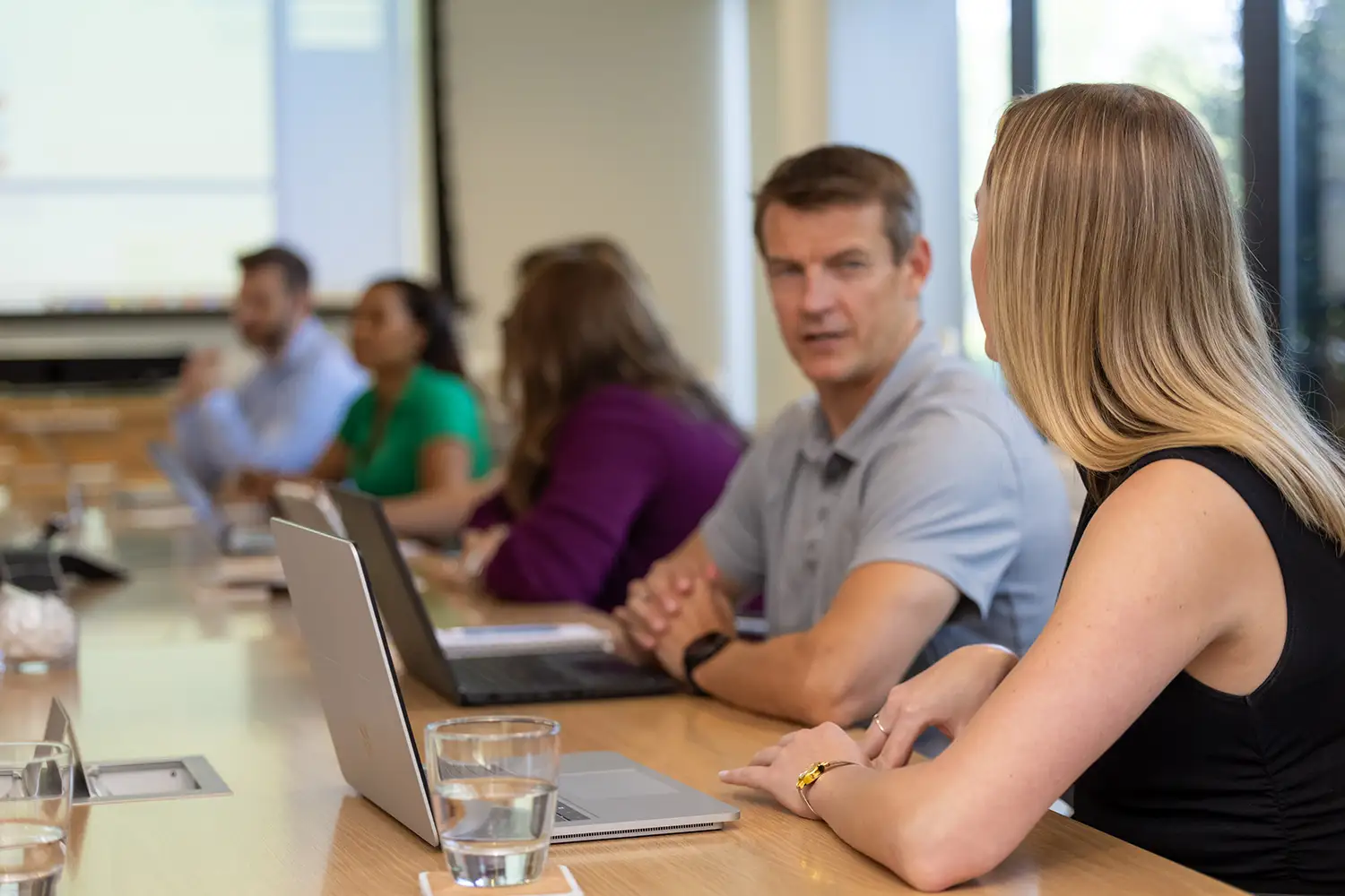 Services leaders focused on their laptops at a shared desk in a collaborative work environment and chatting. 