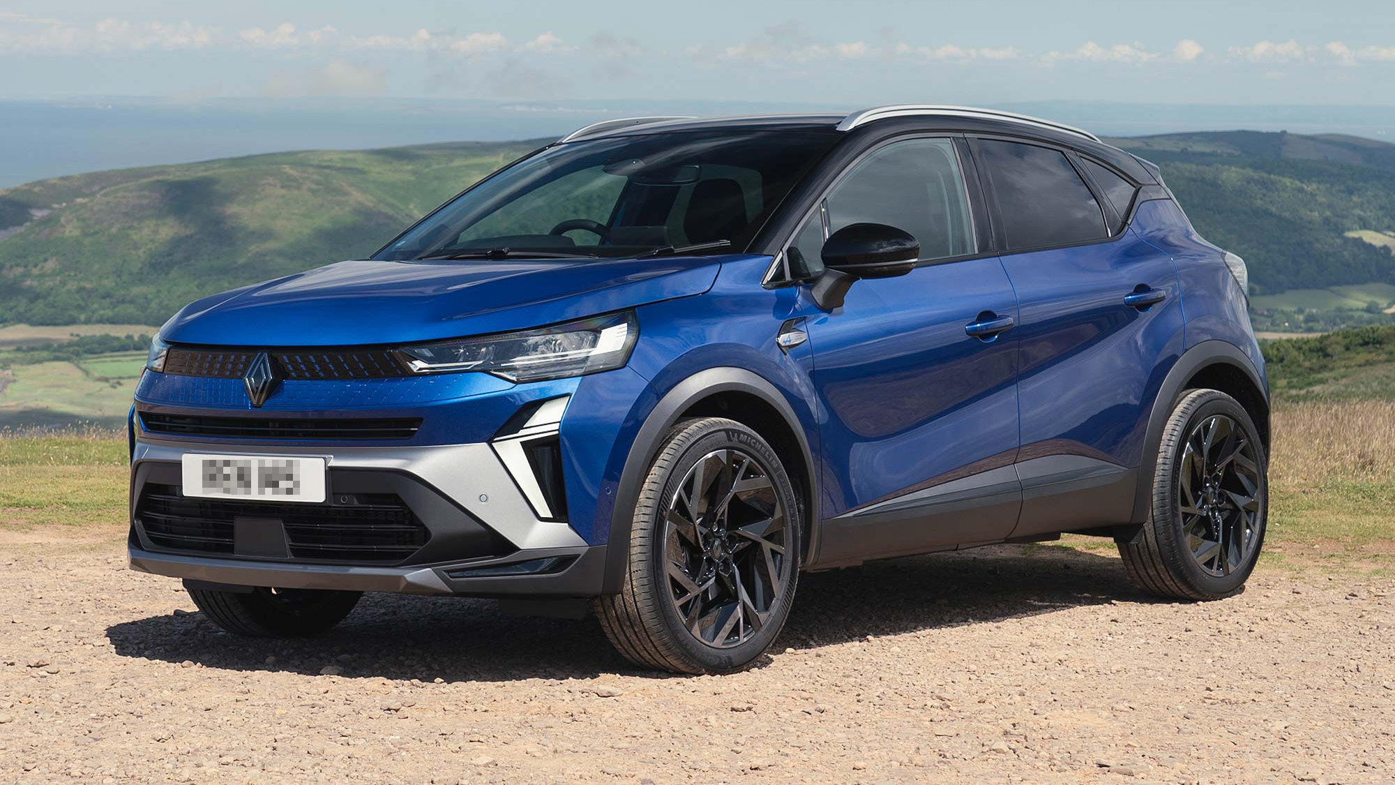 A blue Renault Captur crossover parked on a hilltop with a scenic background, highlighting its angular headlights and sporty stance.