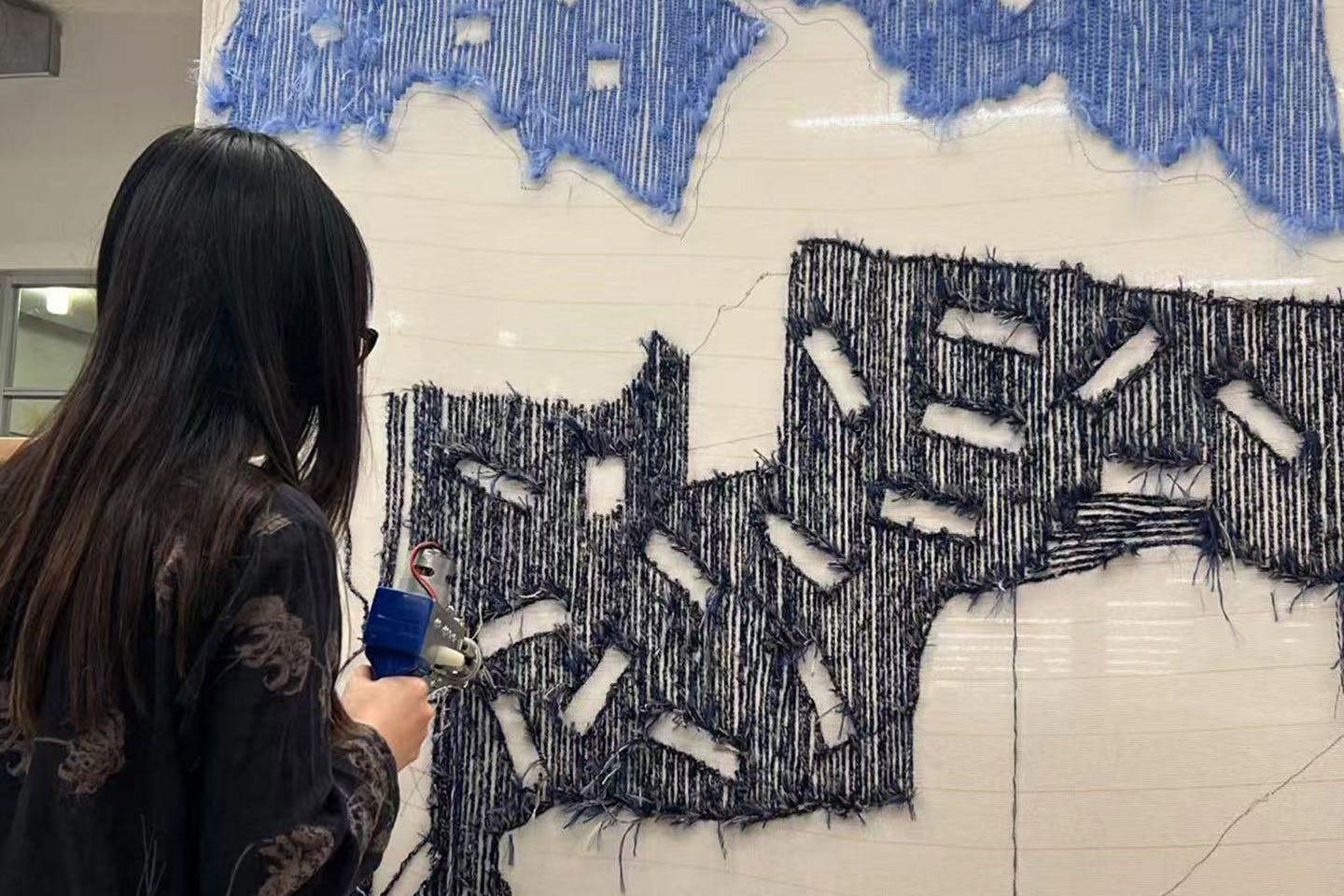 Yichen Pan working on a fiber structure designed to support her tufted map project, which is mounted on the wall.